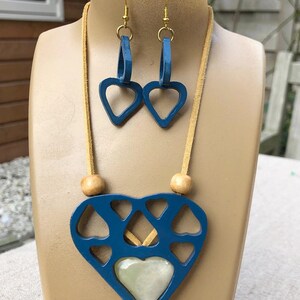 May include: A blue heart-shaped necklace with a smaller white heart in the centre. The necklace is made of wood and has a suede cord. The necklace comes with matching blue heart-shaped earrings.