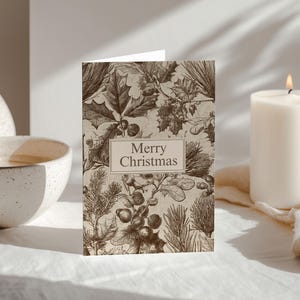 May include: A sepia-toned Christmas card featuring botanical illustrations of holly, oak leaves, and pine needles. The card has the words "Merry Christmas" in a rectangular frame. A lit white candle and a decorative vase are in the background.