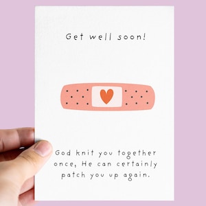 Peut inclure: Une carte blanche avec le texte "Get well soon!" et un pansement de dessin animé avec un cœur. La carte contient également le texte "God knit you together once, He can certainly patch you up again."