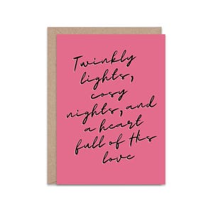 May include: A greeting card with a pink front and a brown back. The pink front has black cursive text that reads: "Twinkly lights, cosy nights, and a heart full of his love."