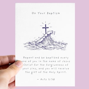 Op de afbeelding: Een witte doopkaart met een blauw kruis boven een golfillustratie. De tekst luidt "Over uw doop" en een bijbelvers uit Handelingen 2:38. Vastgehouden door een hand tegen een lichtpaarse achtergrond.