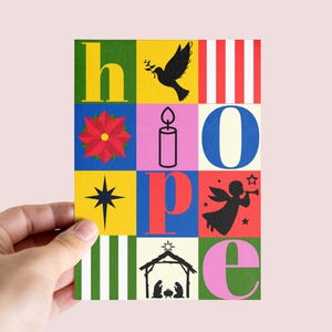 Könnte beinhalten: Eine farbenfrohe Weihnachtskarte mit dem Wort "HOFFNUNG" in einzelnen Blöcken. Jeder Block zeigt ein anderes Bild, darunter eine Taube, ein Weihnachtsstern, eine Kerze, ein Stern, ein Engel und eine Krippenszene. Die Karte wird von einer Hand gehalten.