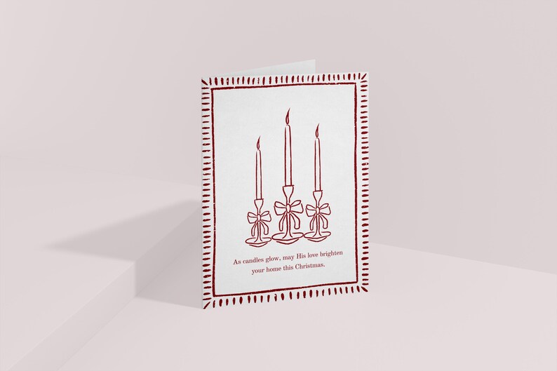 K&ouml;nnte beinhalten: Eine gefaltete Weihnachtskarte mit wei&szlig;em Hintergrund und einem weinroten Rand. Die Karte zeigt eine Strichzeichnung von drei Kerzen mit Schleifen. Der Text unten lautet: &bdquo;M&ouml;ge seine Liebe Ihr Zuhause an diesem Weihnachten erhellen.&ldquo;