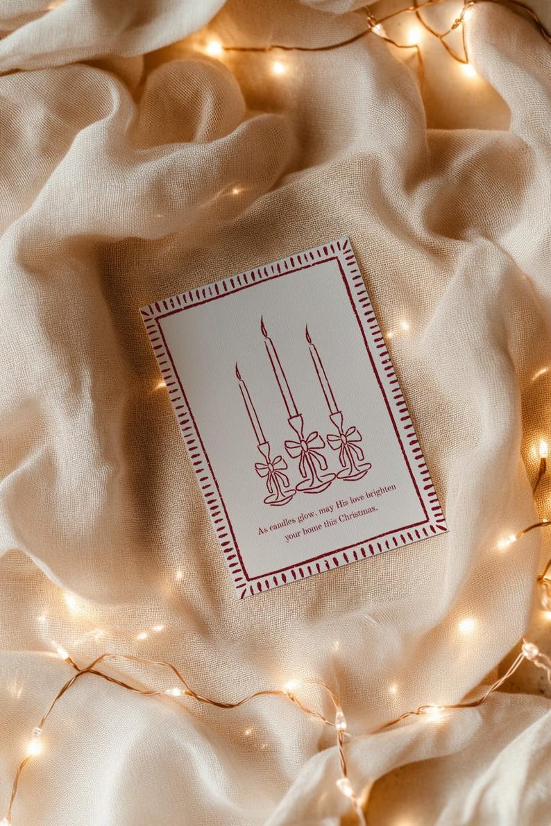 K&ouml;nnte beinhalten: Weihnachtskarte mit roter Umrandung und einer Zeichnung von drei Kerzen auf wei&szlig;em Hintergrund. Der Text lautet: &bdquo;M&ouml;ge seine Liebe Ihr Zuhause an diesem Weihnachten erhellen.&ldquo; Auf beigem Stoff mit Lichterketten.