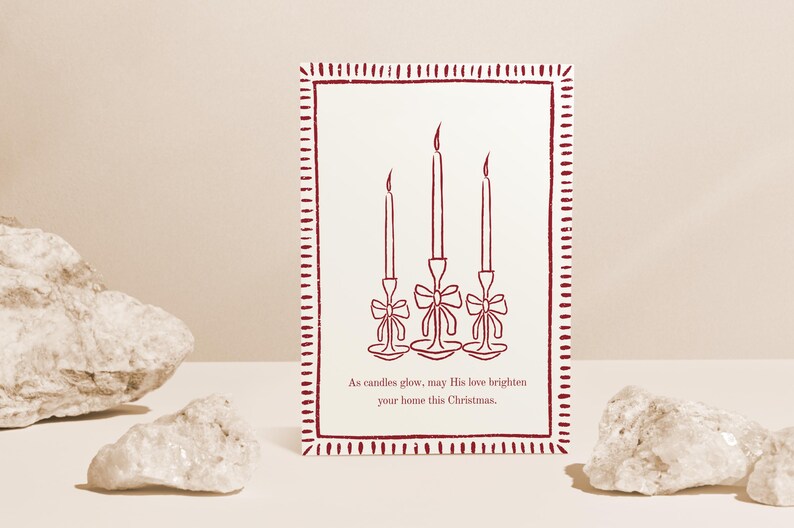 K&ouml;nnte beinhalten: Eine Weihnachtskarte mit einem weinroten Rand und einem cremefarbenen Hintergrund. Die Karte zeigt eine Strichzeichnung von drei Kerzen mit Schleifen. Der Text lautet: &bdquo;Wenn Kerzen leuchten, m&ouml;ge Seine Liebe Ihr Zuhause an diesem Weihnachten erhellen.&ldquo;