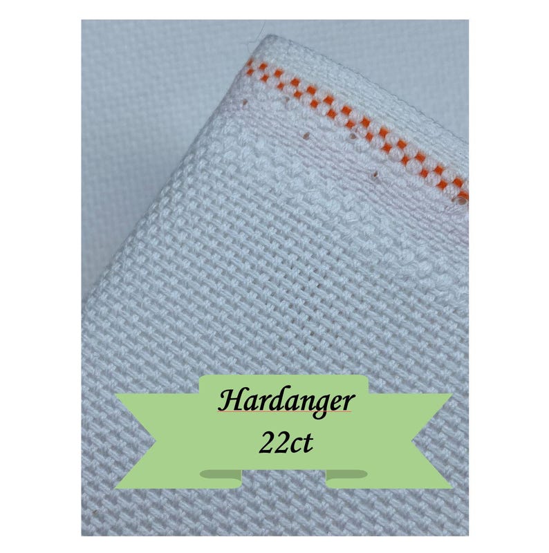 K&ouml;nnte beinhalten: Nahaufnahme eines wei&szlig;en Hardanger-Stoffs mit strukturiertem Gewebe. Der Stoff hat einen Rand mit orangefarbenen N&auml;hten. Der Text "Hardanger 22ct" wird auf einem gr&uuml;nen Banner angezeigt.