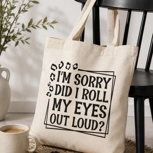 Könnte beinhalten: Eine naturfarbene Stofftasche mit schwarzem Aufdruck I'M SORRY DID I ROLL MY EYES OUT LOUD? Der Text ist von einem dünnen schwarzen rechteckigen Rahmen umgeben, wobei eine dekorative Leopardenmuster-Grafik die obere linke Ecke verziert.