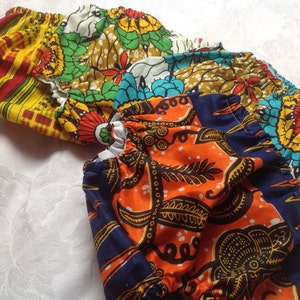 Puede incluir: Tres cubiertas de pañales de tela coloridas con elástico alrededor de las piernas. Las cubiertas están hechas de tela estampada con una variedad de colores, incluyendo naranja, azul, amarillo, verde y rojo.