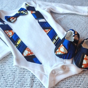 Puede incluir: Un body blanco para bebé con tirantes estampados en azul y naranja y una pajarita a juego. El body se combina con zapatos de bebé estampados en azul y naranja.