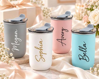 May include: Four cylindrical tumblers with clear lids and light blue flip-top closures. The tumblers are matte gray with white text reading Megan, white with gold text reading Sophia, pink with black text reading Avery, and light blue with black text reading Bella.
