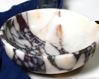 Puede incluir: Un tazón de mármol blanco con patrones de remolino negro y marrón. El tazón es redondo y tiene un acabado liso y pulido.
