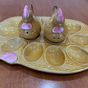 Peut inclure: Un porte-œufs en céramique brun en forme de poule avec deux petits salières et poivrières en forme de poule. Le porte-œufs a six gobelets à œufs individuels et un glaçage moucheté brun et blanc.