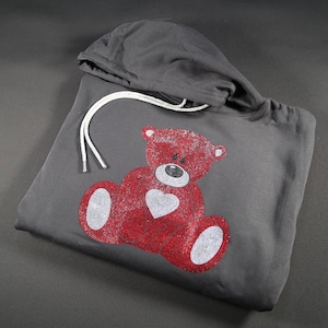 May include: A gray hoodie with a red rhinestone teddy bear holding a heart. The teddy bear is on the front of the hoodie.