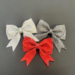 May include: Three sparkly bows in red, silver, and white. The bows are made of shiny material and are perfect for adding a touch of sparkle to any project.