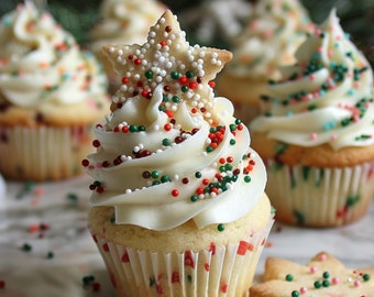May include: A close-up of a cupcake with white frosting, topped with a star-shaped cookie and colorful sprinkles. The cupcake sits in a paper liner with red and green patterns. Other cupcakes are in the background.