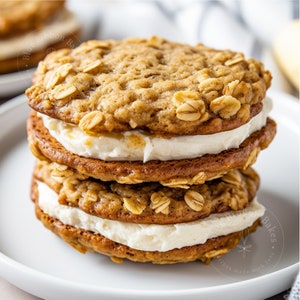 May include: A stack of three oatmeal cookies with a white frosting filling. The cookies are on a white plate. The text "Blue Ribbon Bakes" is visible on the plate.