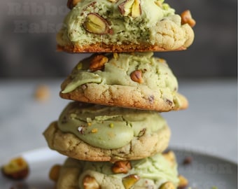 Peut inclure: Une pile de quatre biscuits verts et blancs avec des pistaches et des pépites de chocolat. Les biscuits sont superposés et légèrement flous.