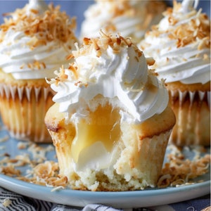 May include: Three cupcakes with white frosting and shredded coconut topping. One cupcake has a bite taken out, revealing a yellow lemon filling.
