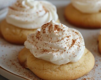 May include: Close-up of three cookies with a white frosting and a sprinkle of cinnamon on top. The cookies are on a white plate.
