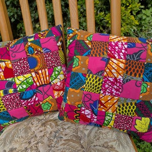 May include: Two square cushions with a patchwork design. The cushions feature a vibrant mix of colours including pink, orange, yellow, and blue. The cushions are placed on a wooden chair with a floral patterned cushion.