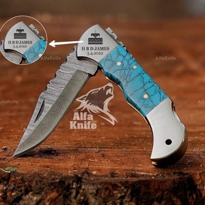 May include: A pocket knife with a blue and white patterned handle and a stainless steel blade. The blade has a damascus pattern and is engraved with the text "HBD JAMES 3.4.2022".