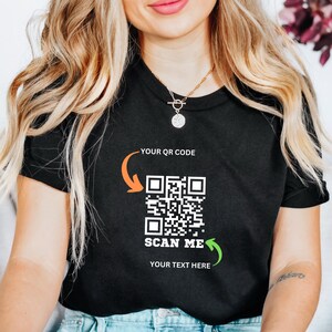 May include: Black t-shirt with a white QR code and the text "SCAN ME" and "YOUR TEXT HERE". The QR code is surrounded by orange and green arrows.