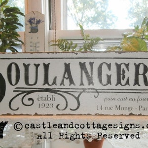 May include: A distressed white wooden sign with the word "BOULANGERIE" in large black letters. The sign includes text in French, including "pain cuit au four frais" and the address "14 rue Monge - Paris, France."