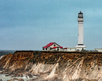 May include: A white lighthouse with a red roof stands on a cliff overlooking the ocean. The lighthouse is tall and slender, with a black lantern on top. The cliff is rocky and brown, and the ocean is blue and choppy.
