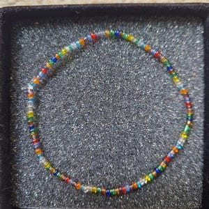 May include: A vibrant beaded bracelet with a spectrum of small, round beads. The bracelet is presented in a black jewellery box, highlighting its colourful design. The beads are approximately 0.6 cm in diameter.