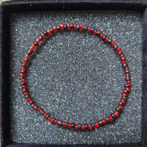 Op de afbeelding: Een rode en zwarte kralen armband in een zwarte fluwelen doos.