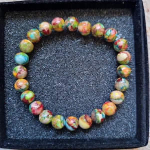 May include: A colorful beaded bracelet featuring round, patterned beads in shades of red, yellow, green, and blue. The bracelet is displayed on a black, textured surface, showcasing the vibrant colors and unique patterns of the beads.