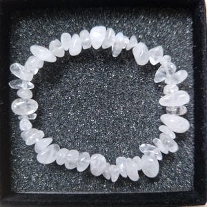 May include: A white crystal bracelet made of small, irregular shaped stones. The bracelet is displayed in a black velvet box.