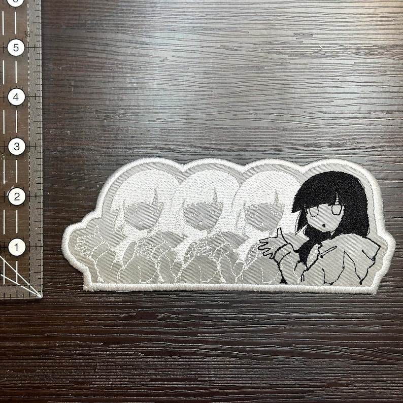 May include: Embroidered patch featuring a cartoon character with black hair and glasses, with three faded images of the same character. The patch is white with black and gray details, and is approximately 3 inches long.