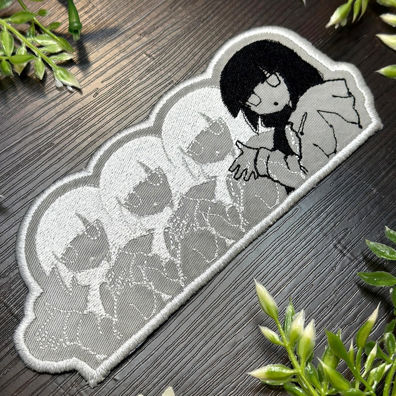 May include: Embroidered patch featuring a stylized anime character with black hair and glasses, extending a hand. The design includes a series of faded character images, all within a gray cloud-shaped border. The patch is gray, black, and white.