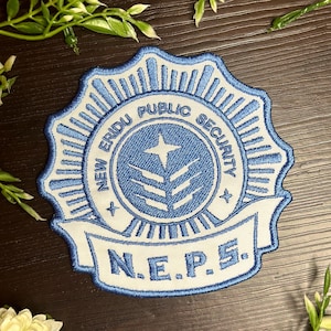 Peut inclure: Un écusson brodé bleu et blanc avec le texte "NEW ERIDU PUBLIC SECURITY" et "N.E.P.S." dans une bannière blanche.