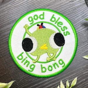 Puede incluir: Parche bordado con un personaje de dibujos animados verde y las palabras "god bless bing bong" en letras verdes. El parche tiene un fondo blanco y un borde verde.