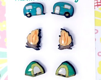 May include: A set of six handmade earrings featuring camping-themed designs. The earrings are made of resin and feature a teal camper, a campfire, and a green tent.