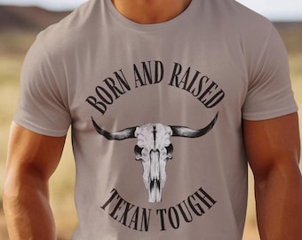 May include: A light brown t-shirt with a black and white bull skull graphic and the text "Born and Raised Texan Tough".