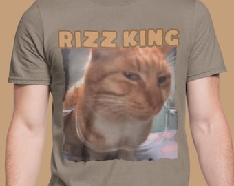 May include: A gray t-shirt with the text "Rizz King" printed in orange on the front. The shirt features a photo of a cat with a serious expression.