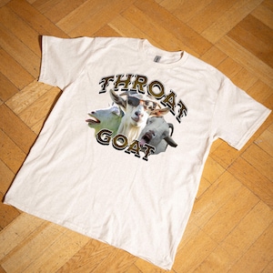 Op de afbeelding: Een wit T-shirt met een afbeelding van drie geiten. De geiten dragen een zonnebril en de tekst "THROAT GOAT" is gedrukt in gouden letters.