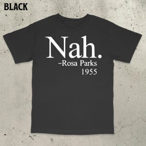 Peut inclure: T-shirt noir avec le mot "Nah" en blanc, suivi de "-Rosa Parks 1955". Le t-shirt est à col rond et à manches courtes.