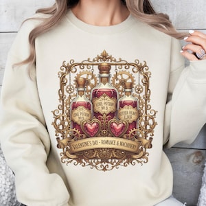 Puede incluir: Sudadera beige con un diseño de San Valentín. El gráfico incluye tres botellas de pociones con etiquetas como "Love Potion No. 9" y "Aether Heart Elixir". Una pancarta dice "Valentine's Day - Romance & Machinery."