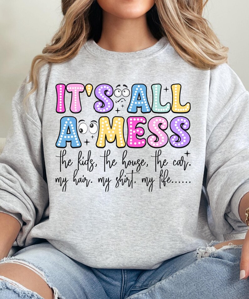 May include: A light gray sweatshirt with the text "IT'S ALL A MESS" in colorful bubble letters. Below the text are the words "the kids, the house, the car. my hair. my shirt. my life....."