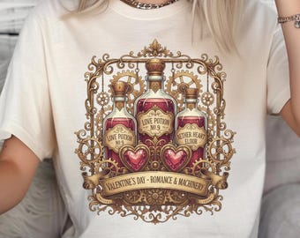May include: Cream-colored t-shirt featuring a detailed graphic. The design includes three potion bottles with labels like "Love Potion No. 9" and "Aether Heart Elixir," set within a decorative frame. A banner reads "Valentine's Day - Romance & Machinery."