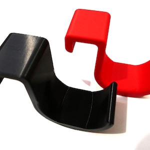 Può includere: Due ganci in plastica, uno nero e uno rosso, progettati per appendere oggetti a una parete o uno scaffale.