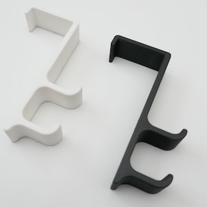 Puede incluir: Dos ganchos de pared, uno blanco y otro negro, con dos ganchos cada uno. Los ganchos son de plástico y tienen un diseño simple y moderno.