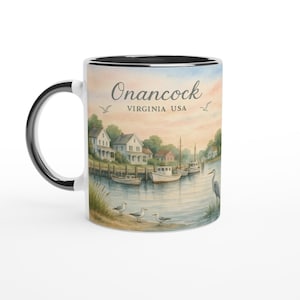 May include: A white ceramic mug with a black handle and rim. The mug features a watercolour illustration of Onancock, Virginia, USA, with boats, houses, and seagulls. The text "Onancock Virginia USA" is printed on the mug.