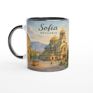 May include: White ceramic mug with a black interior and handle. The mug features a watercolor painting of Sofia, Bulgaria, with the text "Sofia BULGARIA" in a script font. The image includes a church, buildings, and a yellow tram.