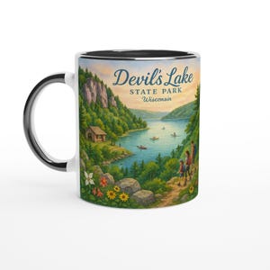 May include: White ceramic mug with a black interior and handle, featuring a scenic illustration of Devil's Lake State Park in Wisconsin. The design includes a lake, trees, and the text "Devil's Lake State Park Wisconsin".
