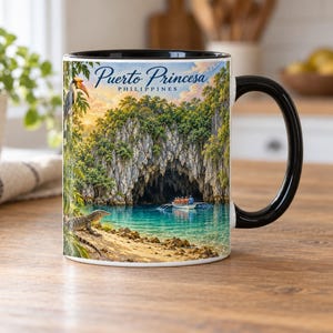 Pode incluir: Uma caneca de cerâmica branca com alça e borda pretas, apresentando uma ilustração colorida do rio subterrâneo de Puerto Princesa nas Filipinas, incluindo um barco com passageiros, um lagarto na margem e um pássaro calau.